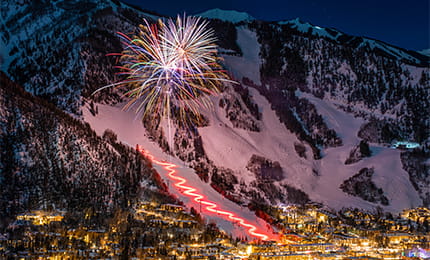 Fireworks lighting up the snow covered Aspen Mountain at night.