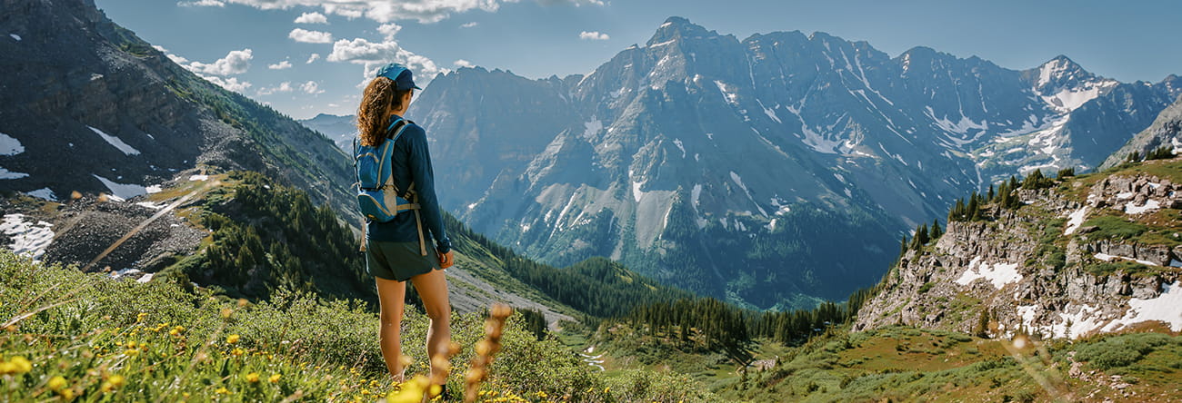 A woman hiking through a field of wildflowers with a jutting mountain range in the background.