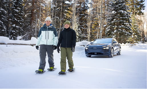 couple snowshoeing in front of audi car