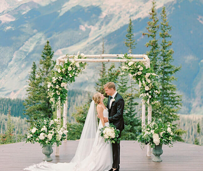 Bride and groom embracing each other under wedding arch on top of Aspen mountain. 