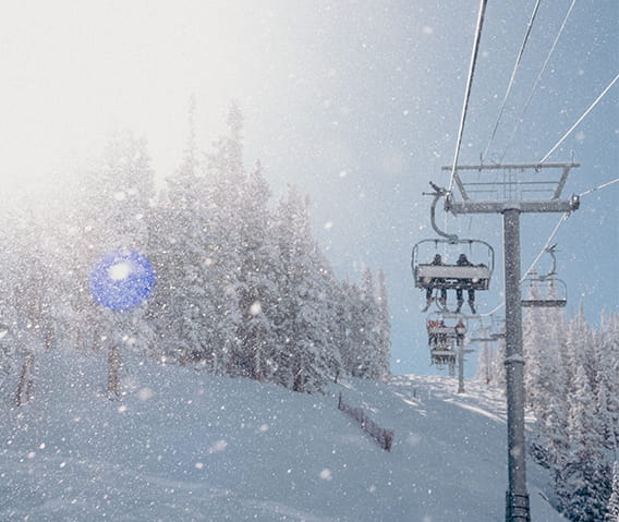 A chairlift with two skiers going up the mountain with gleaming snowflakes all around.