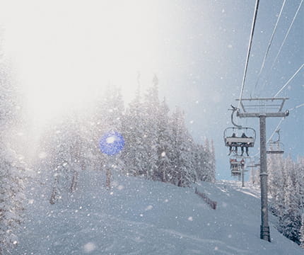 A chairlift with two skiers going up the mountain with gleaming snowflakes all around.