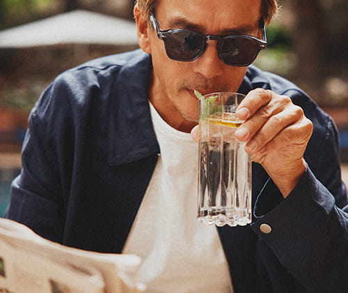 man drinking cocktail reading newspaper