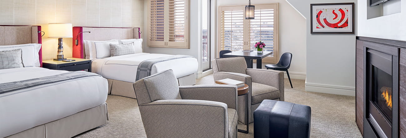 Spacious double queen room with fireplace lit and snow covered trees outside the window.