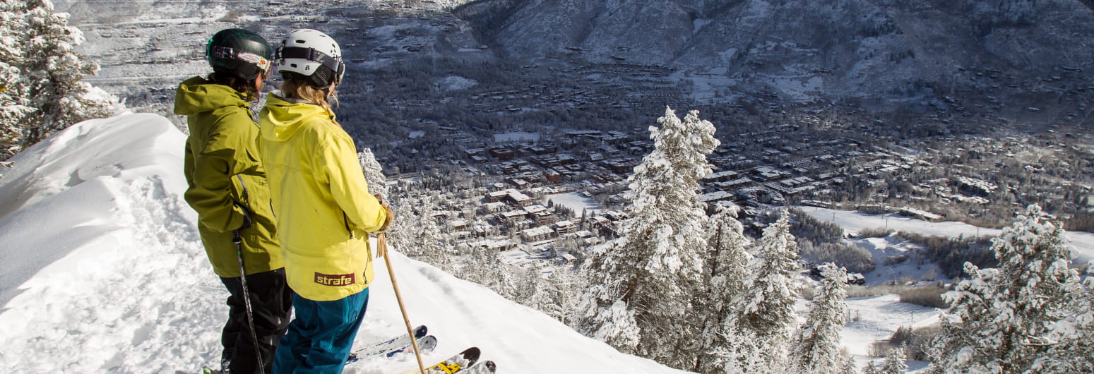 Two skiers standing on a ski slope edge overlooking Aspen town